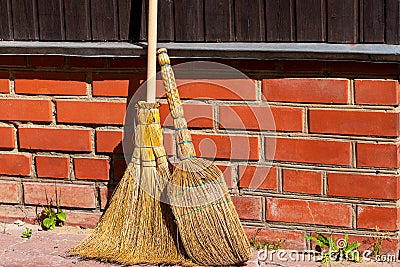 Two brooms on the background of a brick foundation of a rural house in the rays of the bright sun Stock Photo