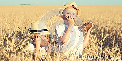 Two brothers eat black round bread on a wheat field. Stock Photo