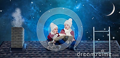 Two brothers sit on Christmas night on the roof and read a book with fairy tales.In anticipation of Christmas miracles. Stock Photo