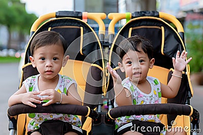 Two brothers sit in a stroller. Adorable twin baby boys sitting in stroller and smiling happily. Childhood emotions. Stock Photo