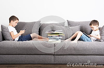Two brothers sits in the opposite side of the sofa and looks on tablet computers. Stock Photo