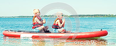 Two brothers swimming on stand up paddle board.Water sports , active lifestyle. Stock Photo