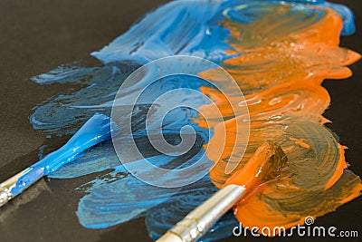 Two brushes and paint strokes on black paper. Blue and orange colors Stock Photo