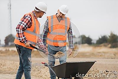 Builders in orange vests and helmets working on the road construction field Stock Photo