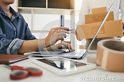 Two business owner are working together to pack products and check customers` orders on their laptops at home Stock Photo