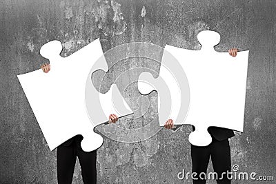 Two business people assembling white jigsaw puzzles with concrete wall Stock Photo