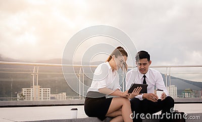 Two business people sitting on roof floor and using digital tablet at outside business office together Stock Photo