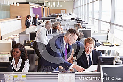 Two businessmen discussing work in a busy, open plan office Stock Photo