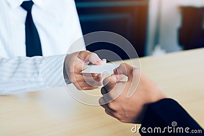 Two businessmen exchanged white business cards on a wooden table Stock Photo