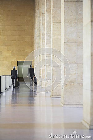 Two Businessmen Pulling Luggage In Airport Lobby Stock Photo