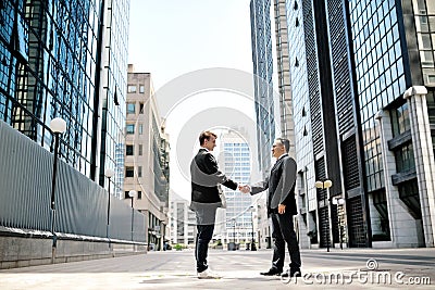 Two businessmen shaking hands on background office corporate buildings Stock Photo