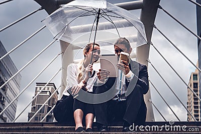 Two businesspeople with umbrella watching tablet and having business discussion in rainy season Stock Photo