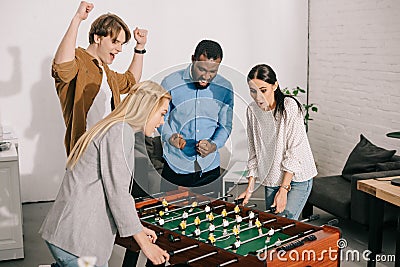 two businesswomen playing table football and male colleagues cheering up them Stock Photo