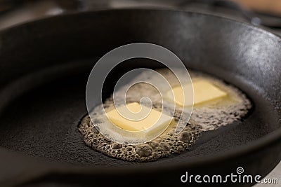 Two butter pats melting on a black cast iron frying pan. Stock Photo