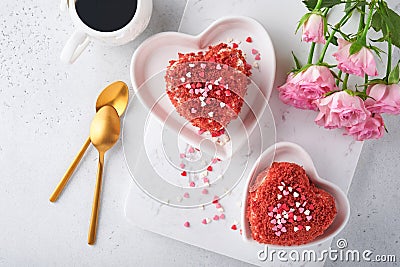 Two cakes Red velvet in shape of hearts on white plate, rose flowers and cup of coffeeon on pink romantic background. Dessert idea Stock Photo