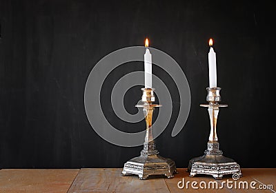 Two candlesticks with burning candels over wooden table and blackboard background Stock Photo