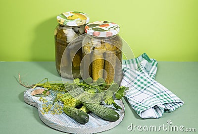 Two cans of pickles and gherkins. Pickled pickles on a round wooden chopping Board with herbs, next to a napkin. Stock Photo