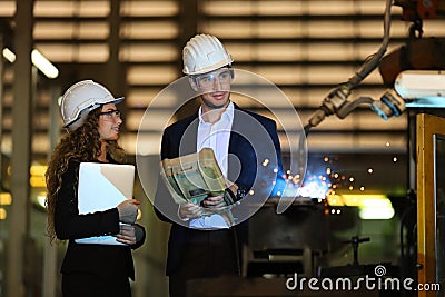 Two Caucasian engineers are inspecting the welding robot machine arm inside factory Stock Photo