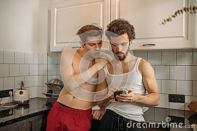 Two gays look at smartphone, in kitchen Stock Photo
