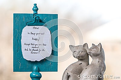 Two ceramic cats sit next to a memory board with a handwritten reminder about happy cats Stock Photo