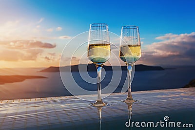 Two champagne glasses on the edge of infinity swimming pool at sunset on Santorini island Stock Photo