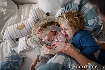 Two small laughing children with unrecognizable father at home, having fun. Stock Photo