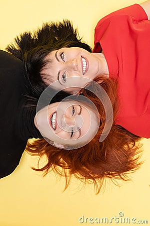 Two cheerful women smiling at camera. Two optimistic women with dark and red hair laughing lying on the floor. Stock Photo