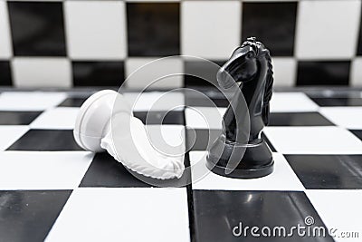 Two chess knights with the vanquished white chess piece lying on its side and the black knight standing upright signifying success Stock Photo