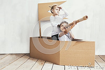 Two children little girls home in a cardboard ship play captains Stock Photo