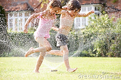 Two Children Running Through Garden Sprinkler Stock Photo