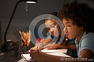 Two Children Studying At Desk In Bedroom In Evening Stock Photo