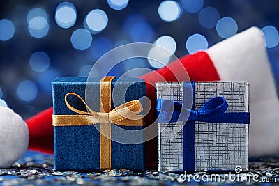 Two christmas gift box or present and santa hat against blue bokeh background. Magic holiday greeting card. Stock Photo