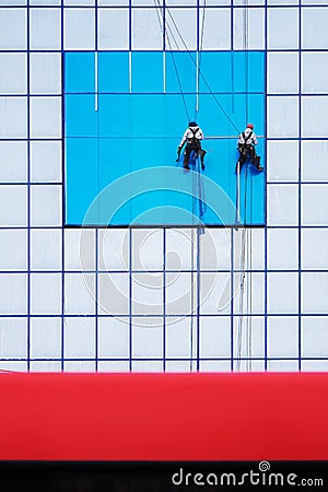 Two climbers on a blue office building hang a banner Stock Photo