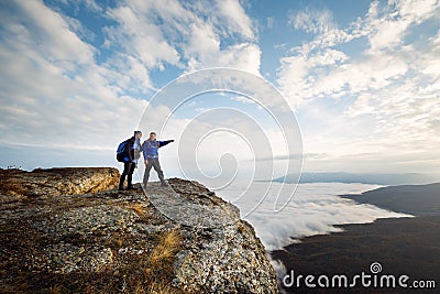 Two climbers standing on top of summit above clouds in the mountains. Hiker man pointing with his hand discussing route Stock Photo