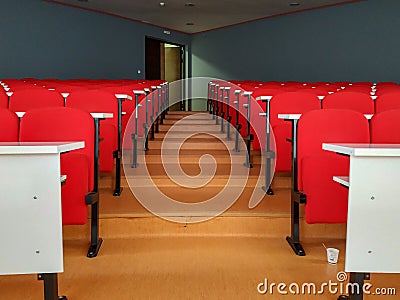 Two columns of amphitheater lecture university or conference big room rows of red chairs and white tables aligned with path in Stock Photo