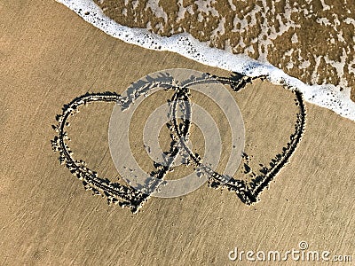 Two connected Hearts drawn on the beach sand with sea waves Stock Photo