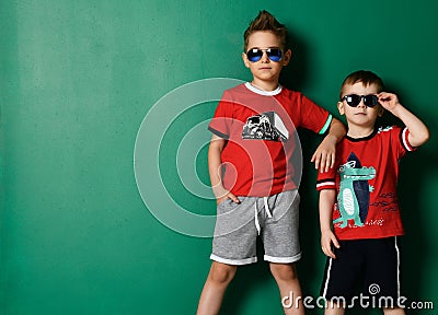 Two cool boys best friends in modern summer wear shorts, red t-shirt with prints and sunglasses posing together Stock Photo