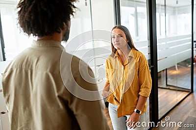 Two coworkers chatting during coffee break standing in glass hall of office building. Curly african-american male Stock Photo