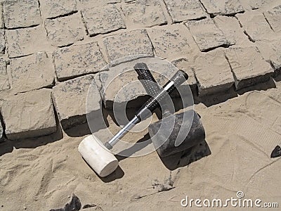 Two crossed rubber hammers lie on the unfinished laying of granite paving stones Stock Photo