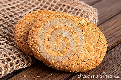 Two crunchy oat and wholemeal biscuits lying on brown burlap on dark wood Stock Photo