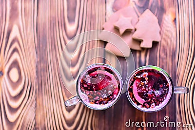 Two cups of red mulled vine with spices, citrus fruits and tasty gingerbreads lying on dark wooden table. Top view. Copy space/ Stock Photo