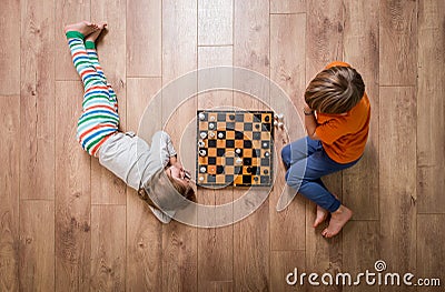 Two cute children playing chess at home while lying on floor. Boy and girl. Win and lost game. Win win. Stock Photo
