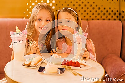 Two cute girlfriends in a cafe. Girls with cake and unicorn cocktail Stock Photo