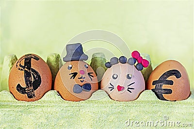 two cute hare eggs in a black hat and with a red plasticine bow in an egg container with euro and dollar on the sides on a light Stock Photo