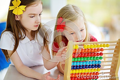 Two cute little girls playing with abacus at home. Big sister teaching her sibling to count. Stock Photo