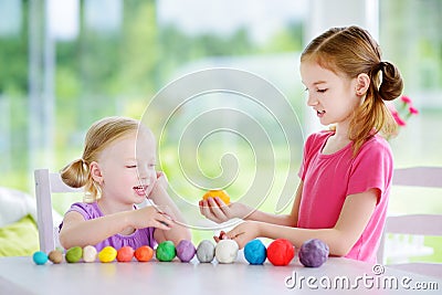 Two cute little sisters having fun together with colorful modeling clay at a daycare Stock Photo
