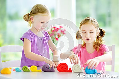 Two cute little sisters having fun together with colorful modeling clay at a daycare Stock Photo