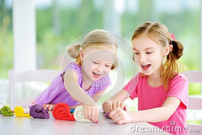 Two cute little sisters having fun together with colorful modeling clay at a daycare Stock Photo