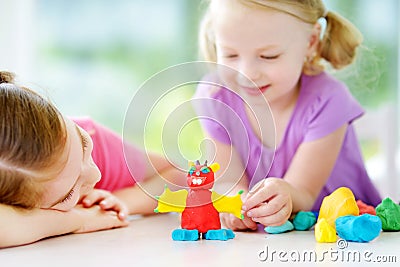 Two cute little sisters having fun together with colorful modeling clay at a daycare. Creative kids molding at home. Stock Photo