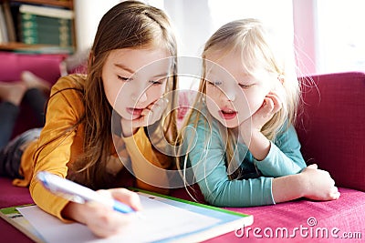 Two cute little sisters writing a letter together at home. Older sister helping youngster with her homework. Stock Photo